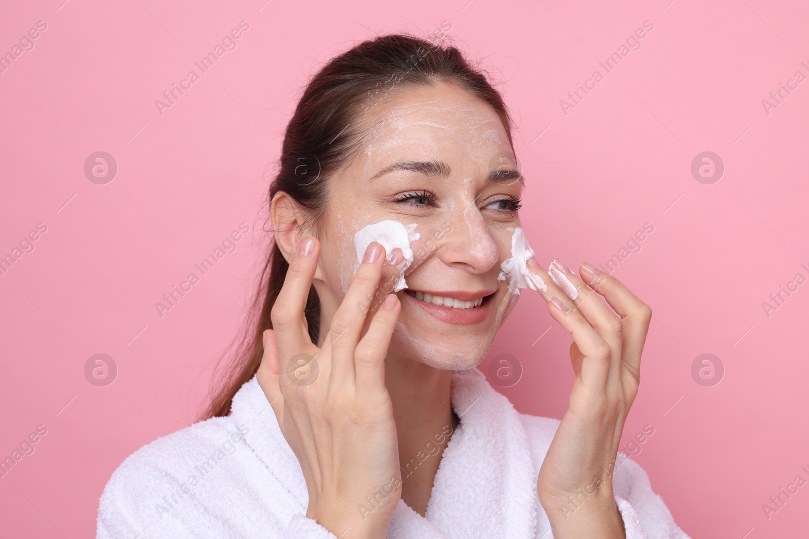 Photo of Spa day. Beautiful woman applying mask onto her face on pink background