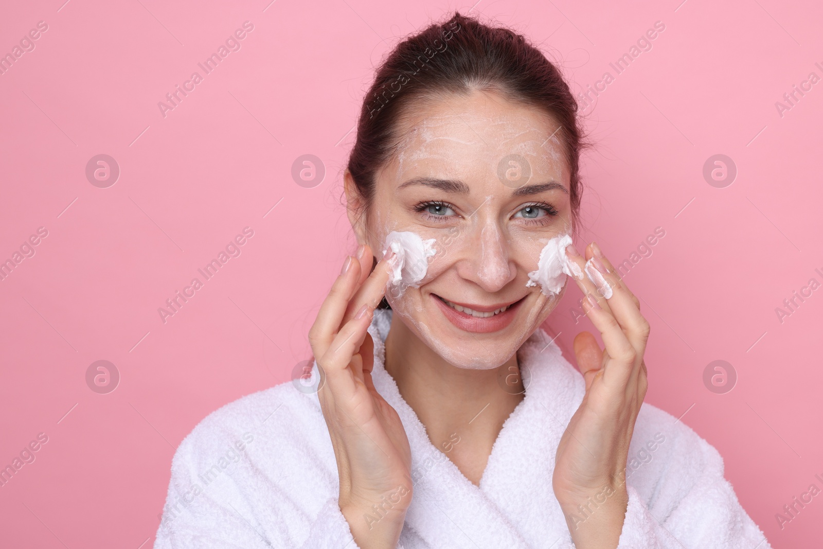 Photo of Spa day. Beautiful woman applying mask onto her face on pink background