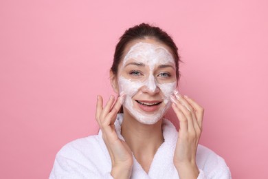 Photo of Spa day. Beautiful woman applying mask onto her face on pink background