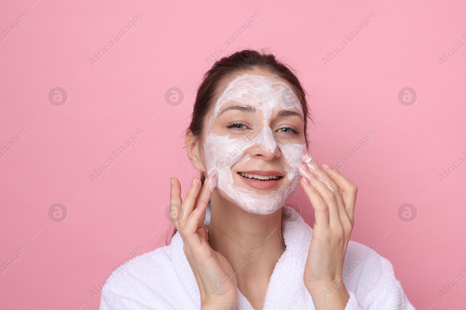 Photo of Spa day. Beautiful woman applying mask onto her face on pink background