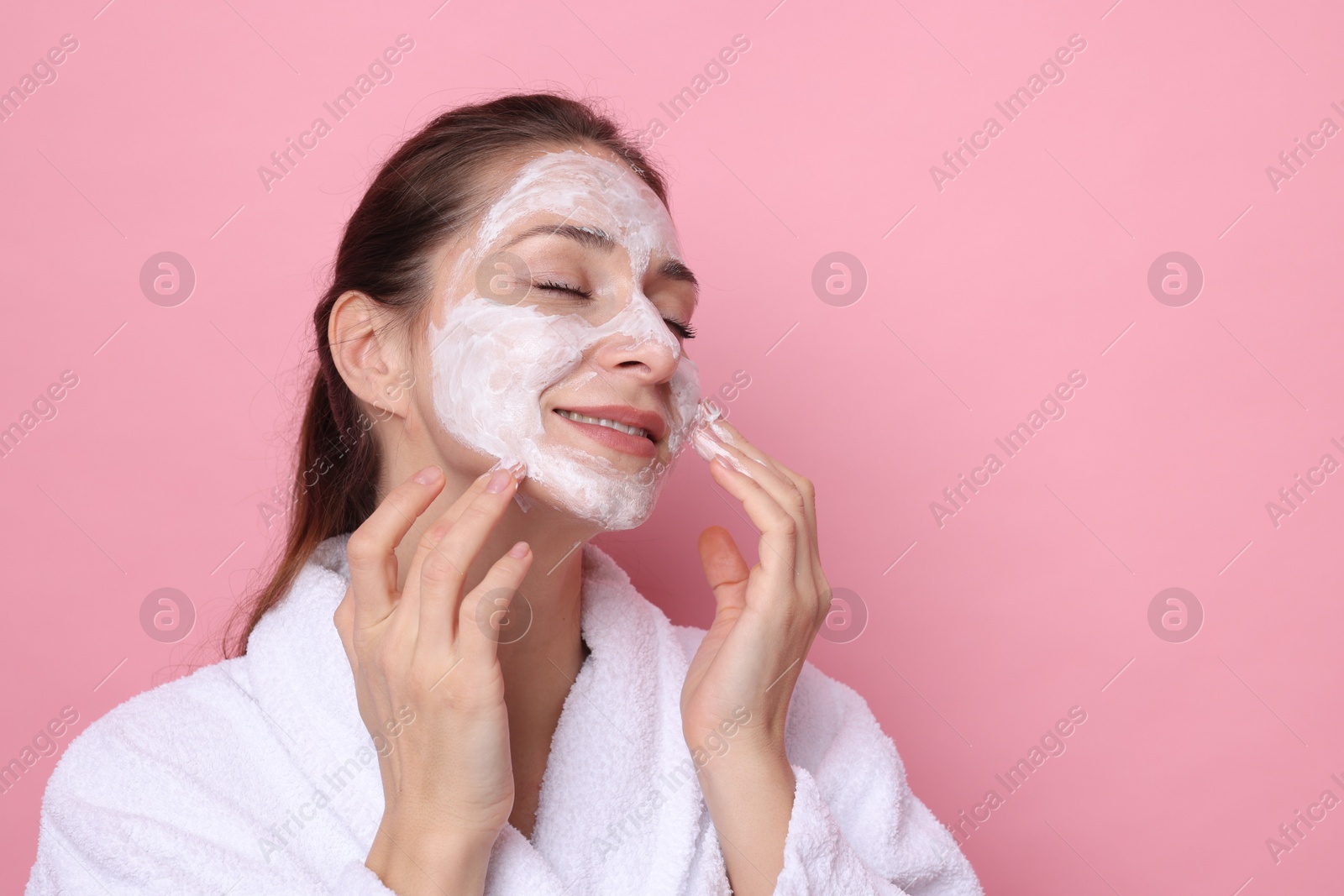 Photo of Spa day. Beautiful woman applying mask onto her face on pink background, space for text