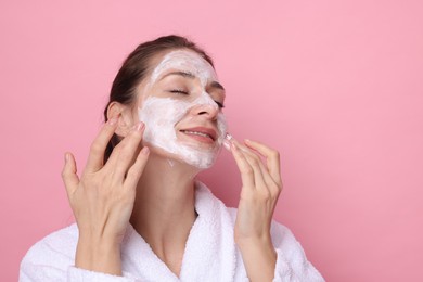 Photo of Spa day. Beautiful woman applying mask onto her face on pink background, space for text