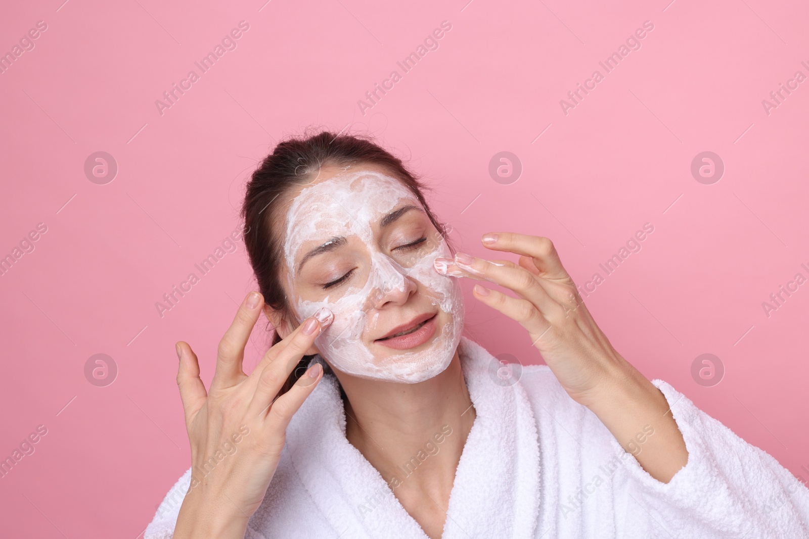 Photo of Spa day. Beautiful woman applying mask onto her face on pink background