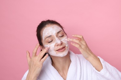 Photo of Spa day. Beautiful woman applying mask onto her face on pink background