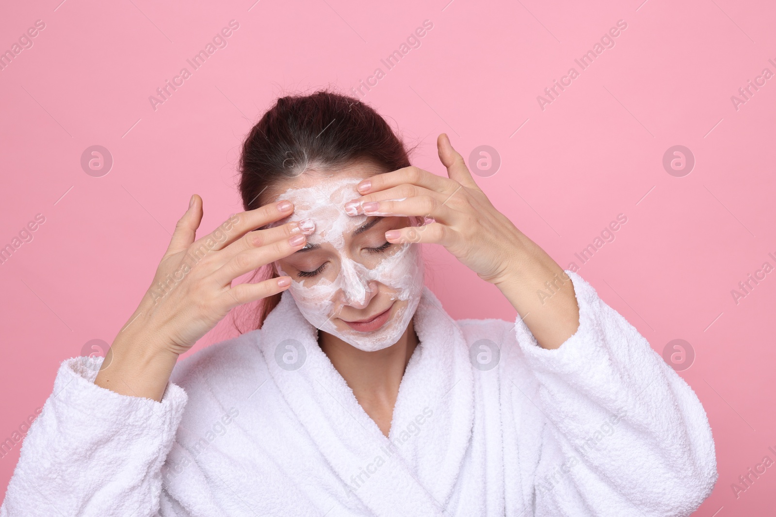 Photo of Spa day. Beautiful woman applying mask onto her face on pink background