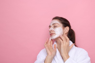 Photo of Spa day. Beautiful woman applying mask onto her face on pink background, space for text