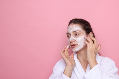 Photo of Spa day. Beautiful woman applying mask onto her face on pink background, space for text