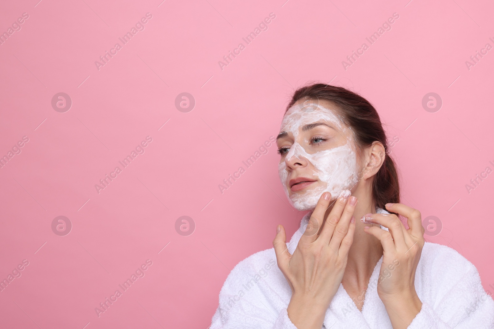 Photo of Spa day. Beautiful woman applying mask onto her face on pink background, space for text