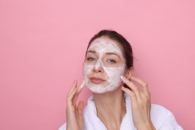 Photo of Spa day. Beautiful woman applying mask onto her face on pink background