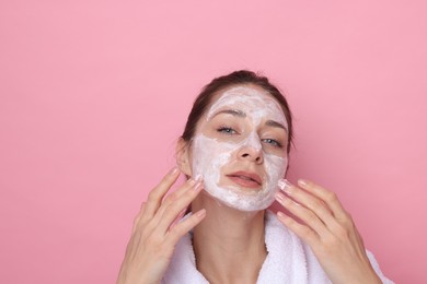 Photo of Spa day. Beautiful woman applying mask onto her face on pink background