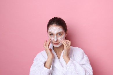 Photo of Spa day. Beautiful woman applying mask onto her face on pink background