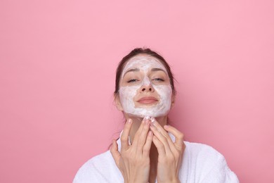 Photo of Spa day. Beautiful woman applying mask onto her face on pink background