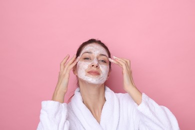 Photo of Spa day. Beautiful woman applying mask onto her face on pink background