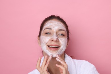 Photo of Spa day. Beautiful woman applying mask onto her face on pink background