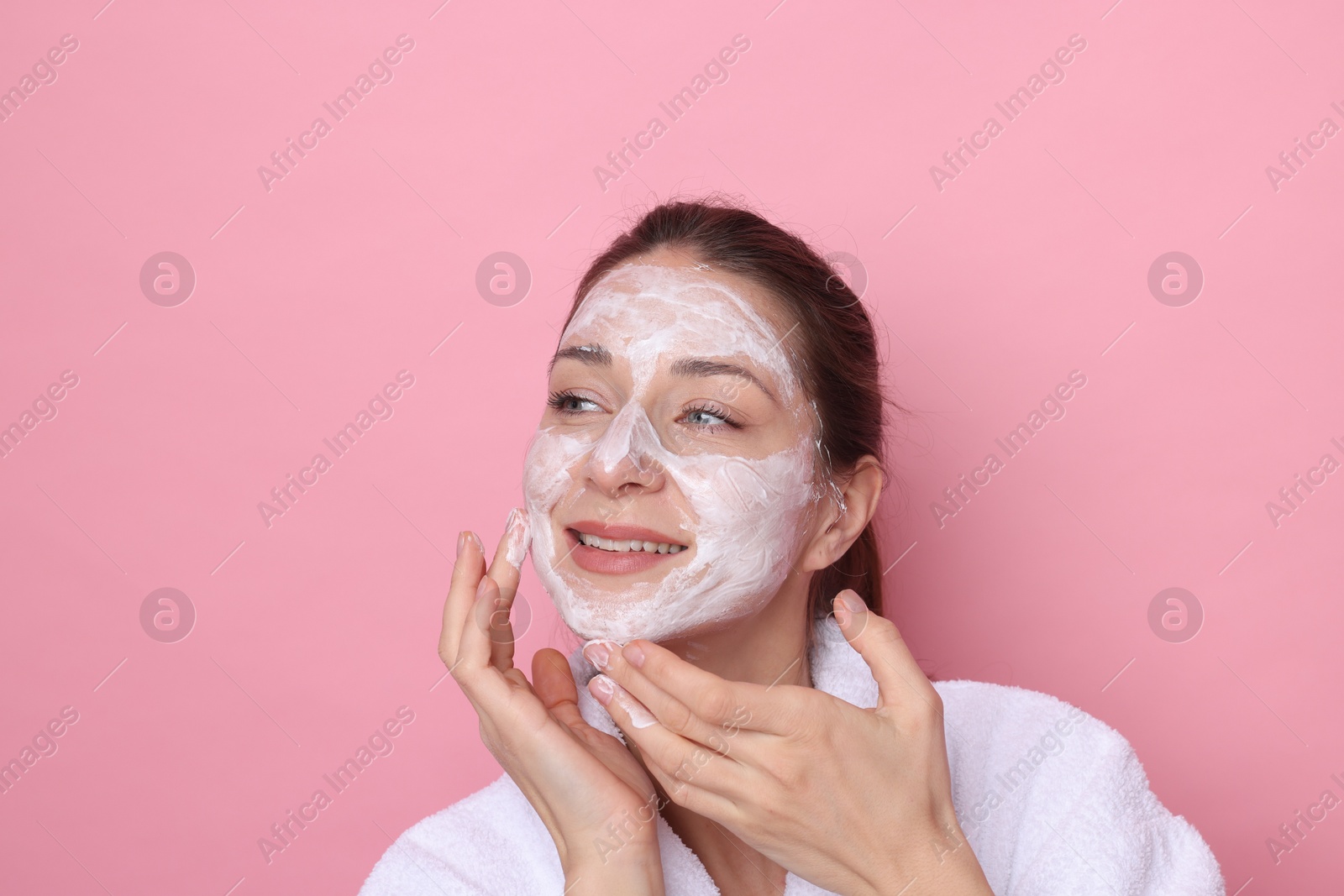 Photo of Spa day. Beautiful woman applying mask onto her face on pink background