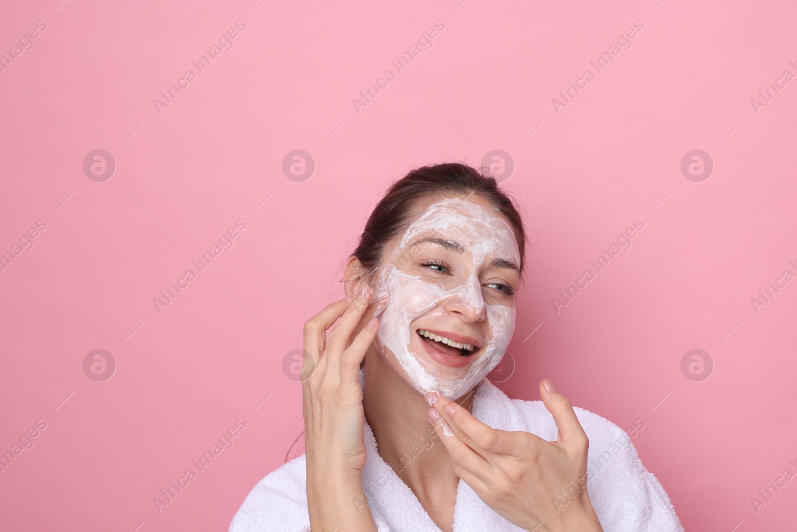 Photo of Spa day. Beautiful woman applying mask onto her face on pink background