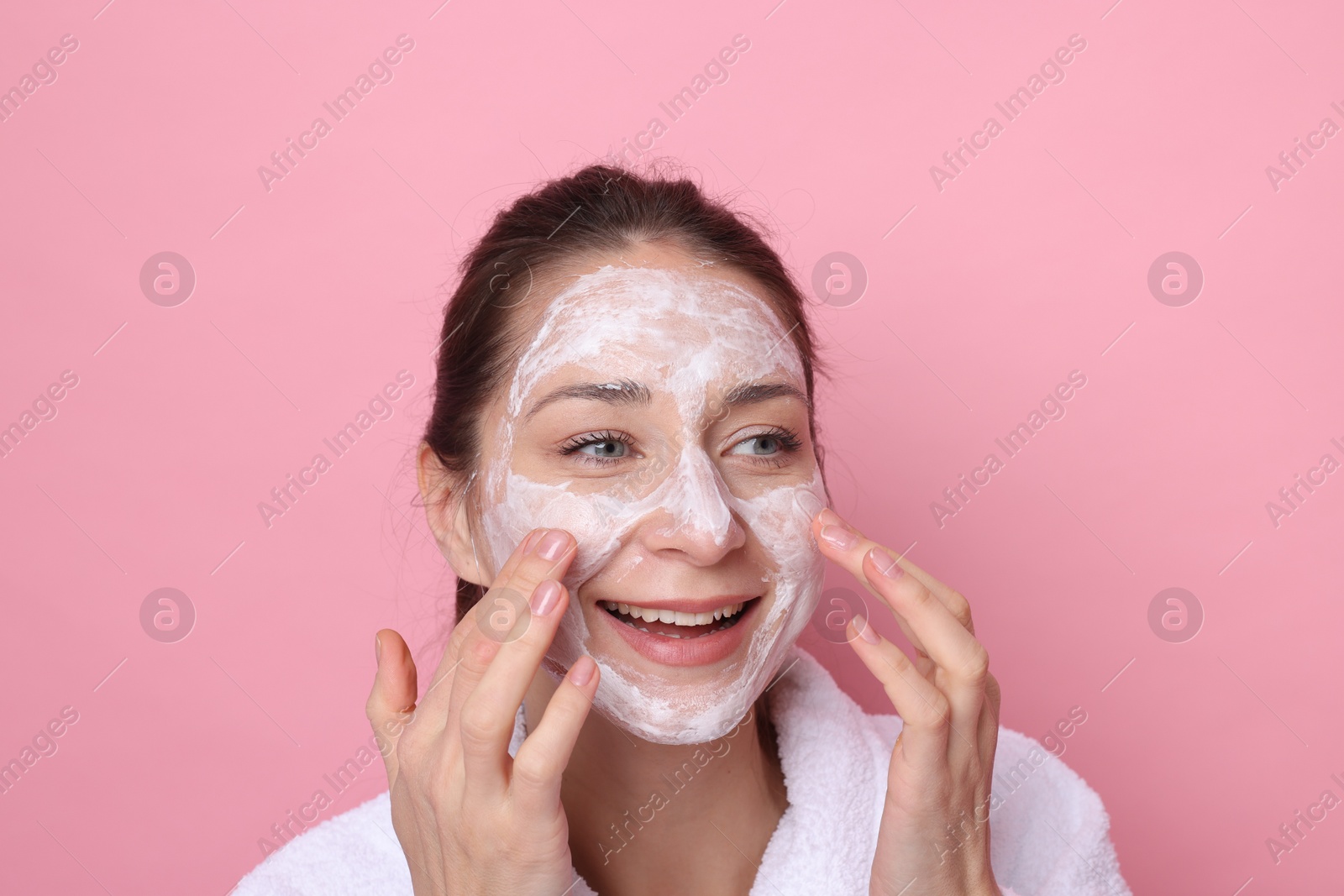 Photo of Spa day. Beautiful woman applying mask onto her face on pink background