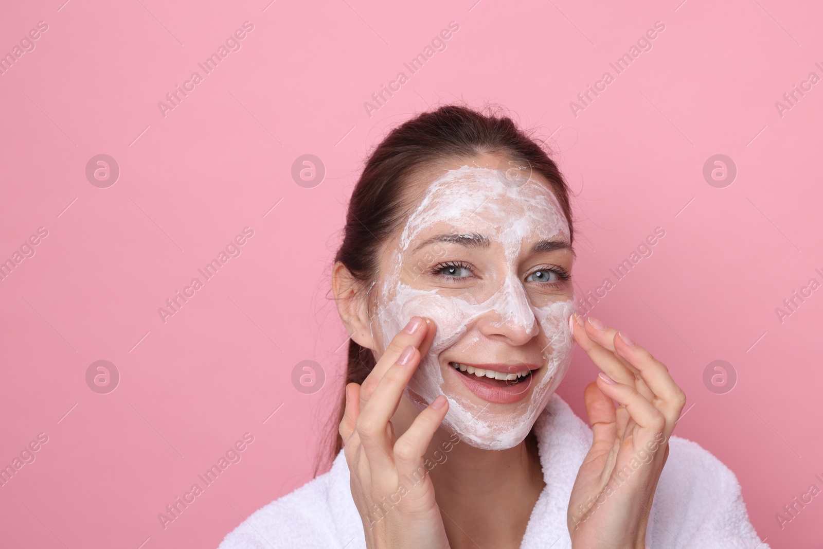 Photo of Spa day. Beautiful woman applying mask onto her face on pink background