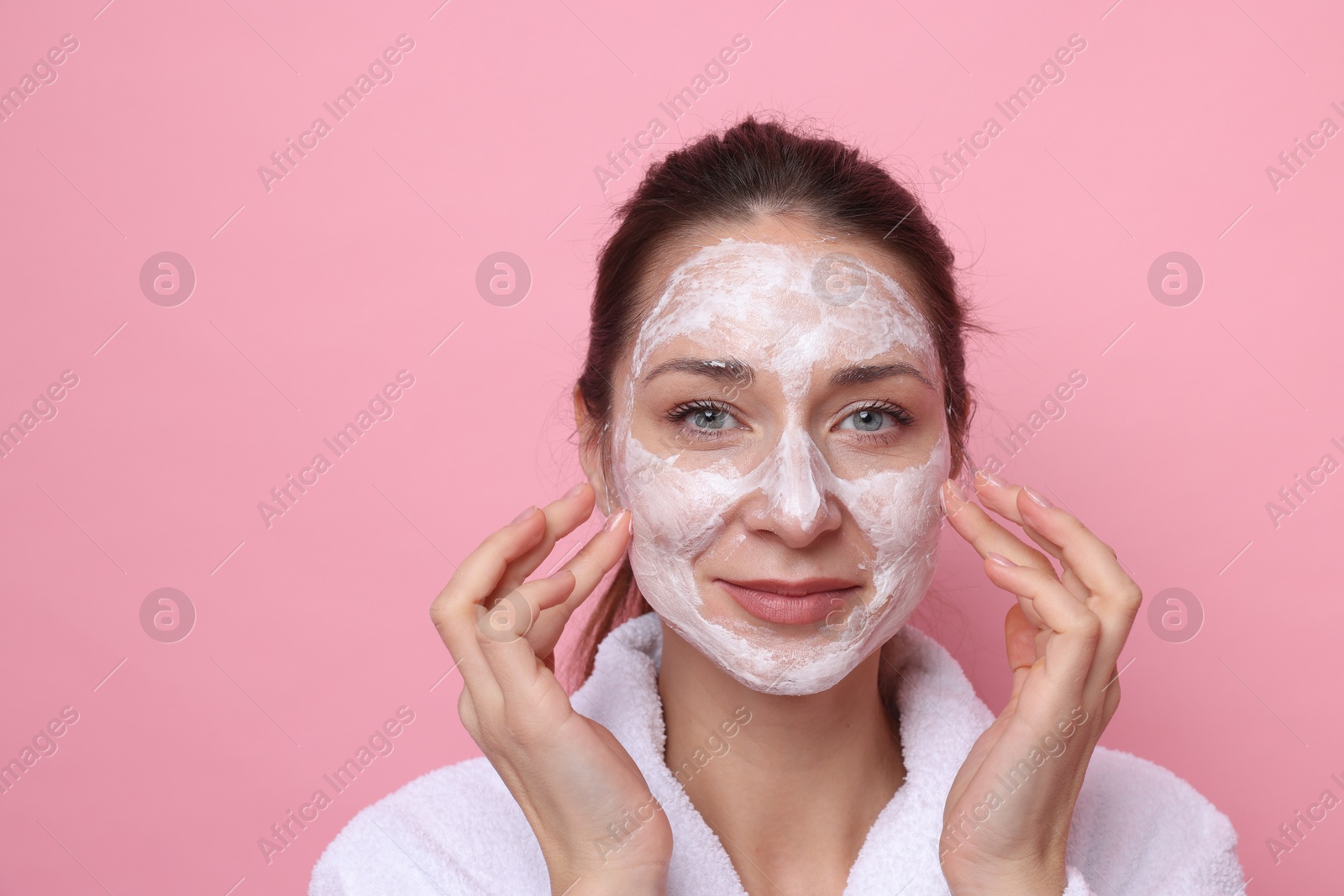 Photo of Spa day. Beautiful woman applying mask onto her face on pink background