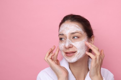 Photo of Spa day. Beautiful woman applying mask onto her face on pink background