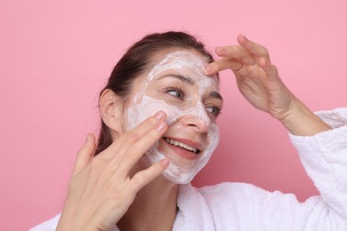 Photo of Spa day. Beautiful woman applying mask onto her face on pink background