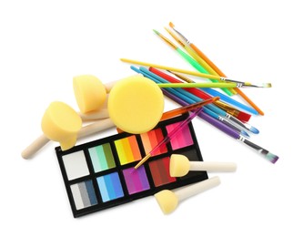 Photo of Bright face paint palette, brushes and sponges isolated on white, top view