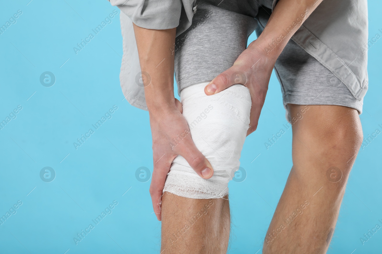 Photo of Man with medical bandage on his knee against light blue background, closeup. Space for text