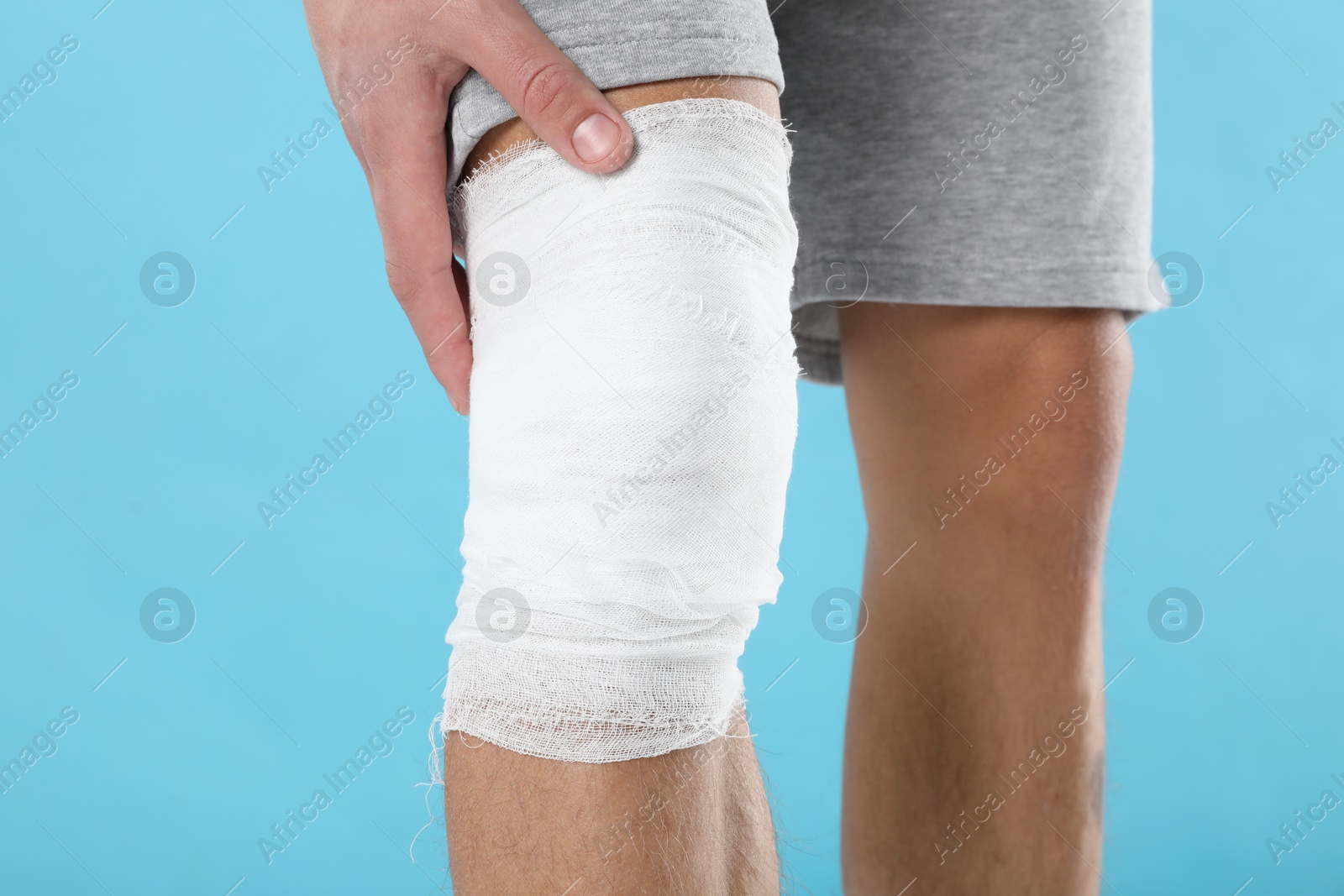 Photo of Man with medical bandage on his knee against light blue background, closeup