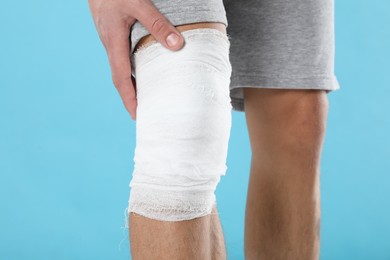 Photo of Man with medical bandage on his knee against light blue background, closeup