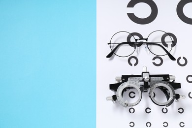 Photo of Glasses, trial frame and vision test chart on light blue background, flat lay. Space for text