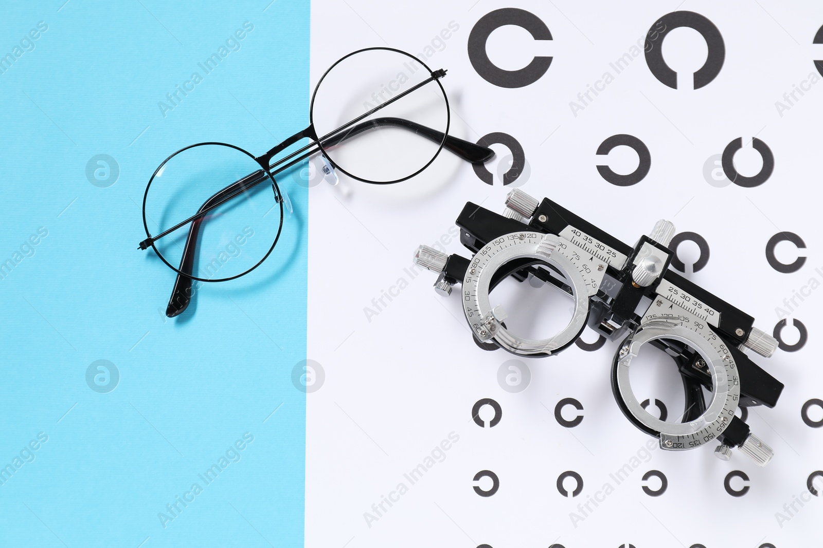 Photo of Glasses, trial frame and vision test chart on light blue background, flat lay