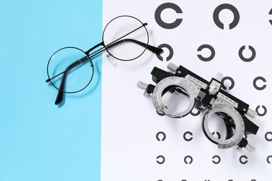 Photo of Glasses, trial frame and vision test chart on light blue background, flat lay