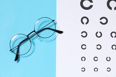 Photo of Glasses and vision test chart on light blue background, flat lay