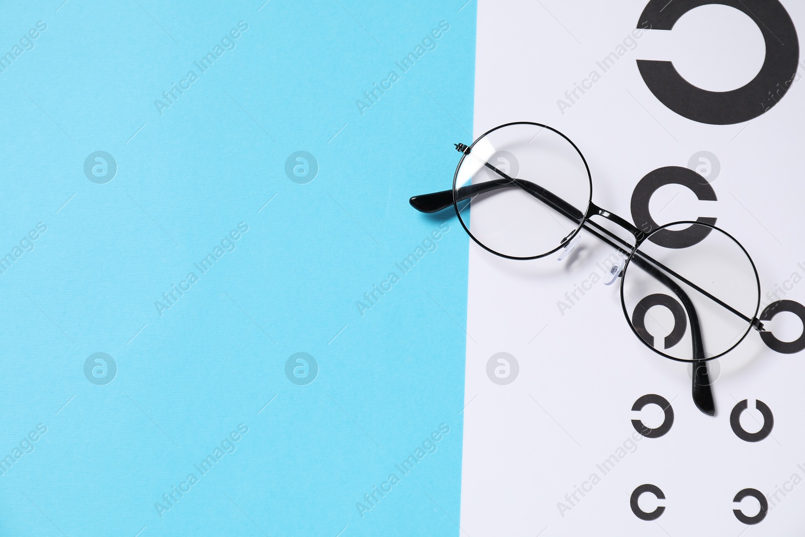 Photo of Glasses and vision test chart on light blue background, top view. Space for text