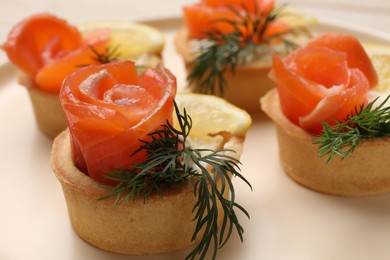 Photo of Tasty tartlets with salmon, lemon and dill on plate, closeup