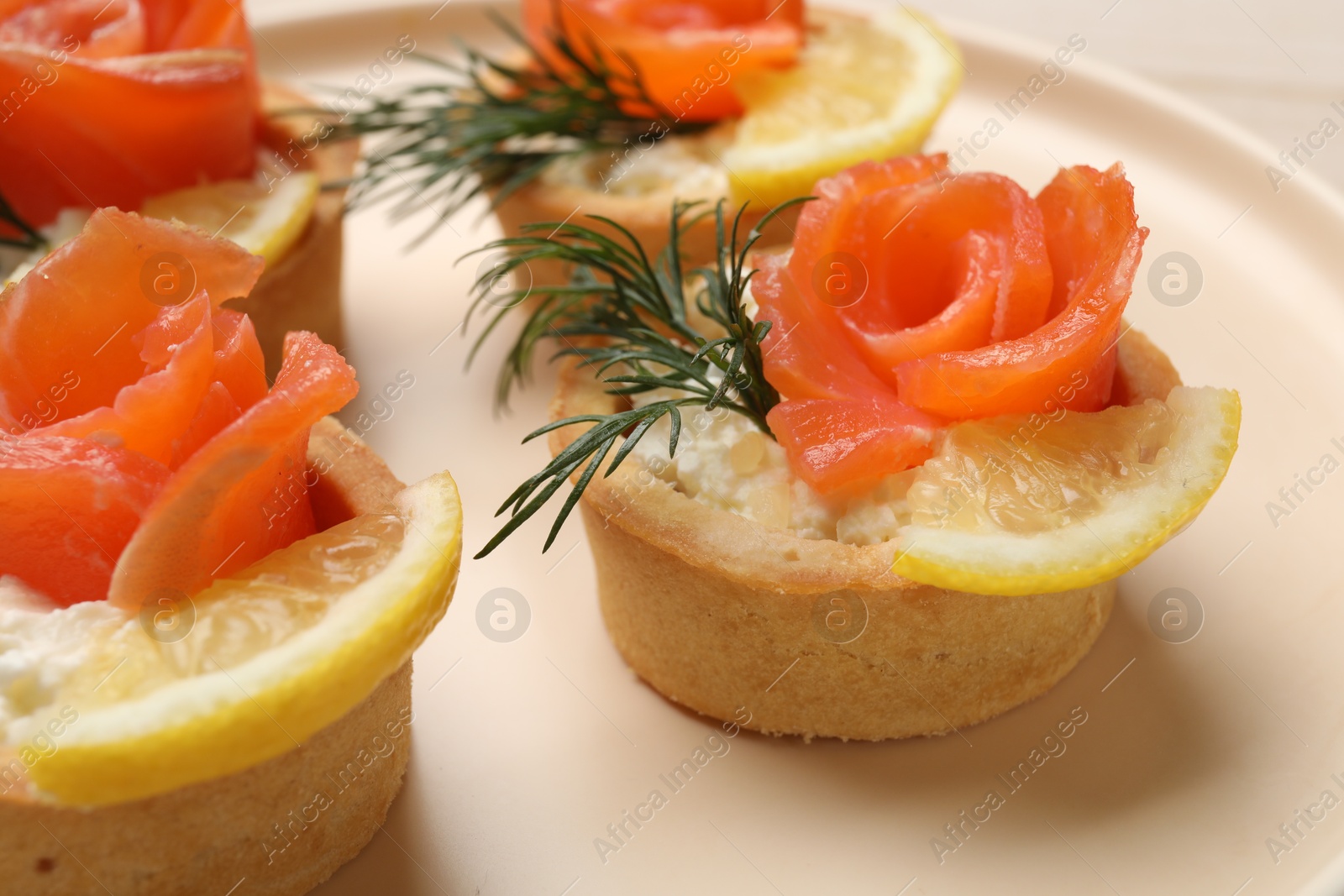 Photo of Tasty tartlets with salmon, lemon and dill on plate, closeup