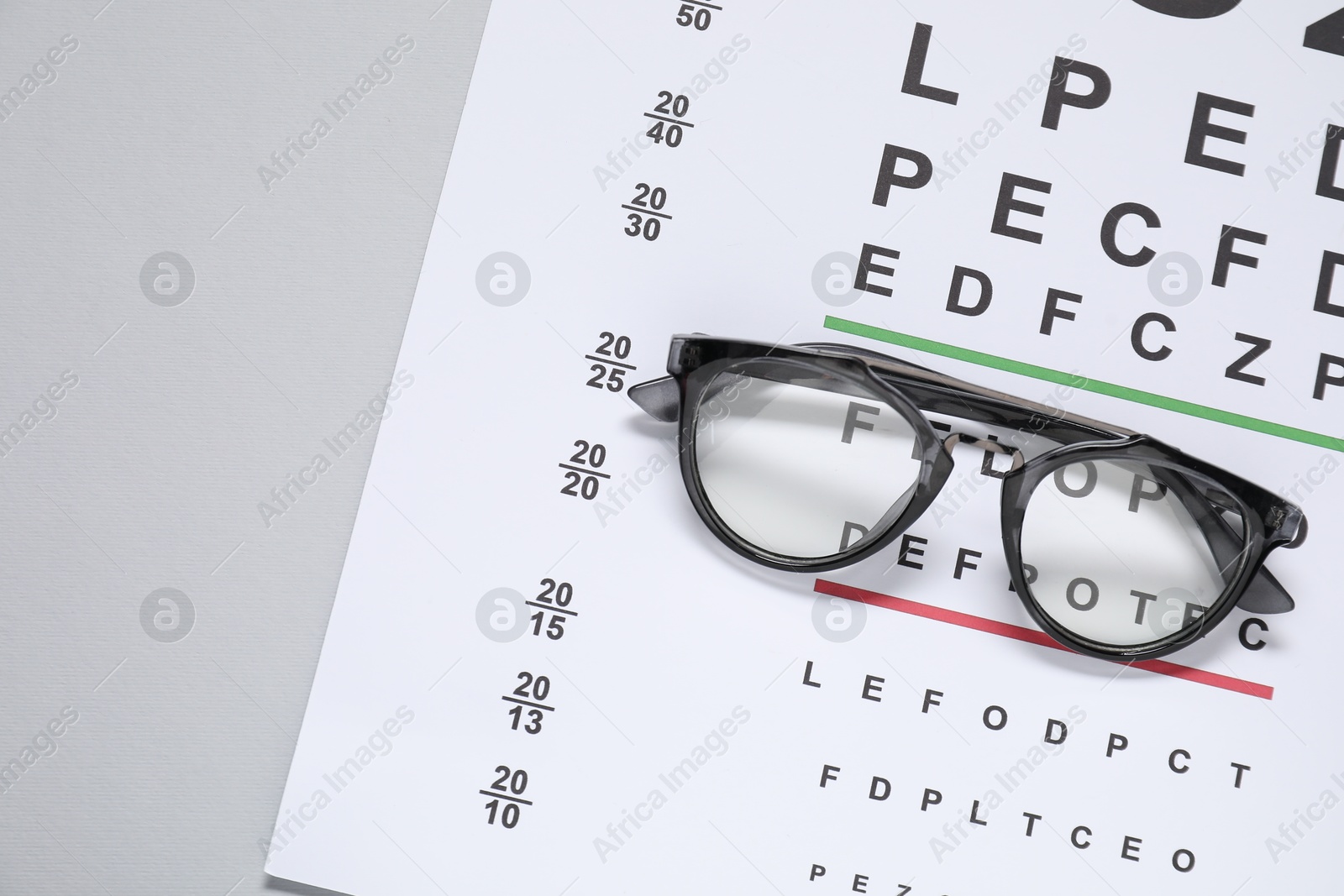 Photo of Glasses and vision test chart on gray background, top view. Space for text