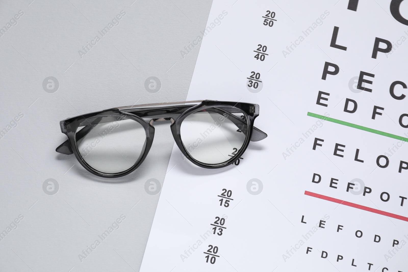 Photo of Glasses and vision test chart on gray background, top view