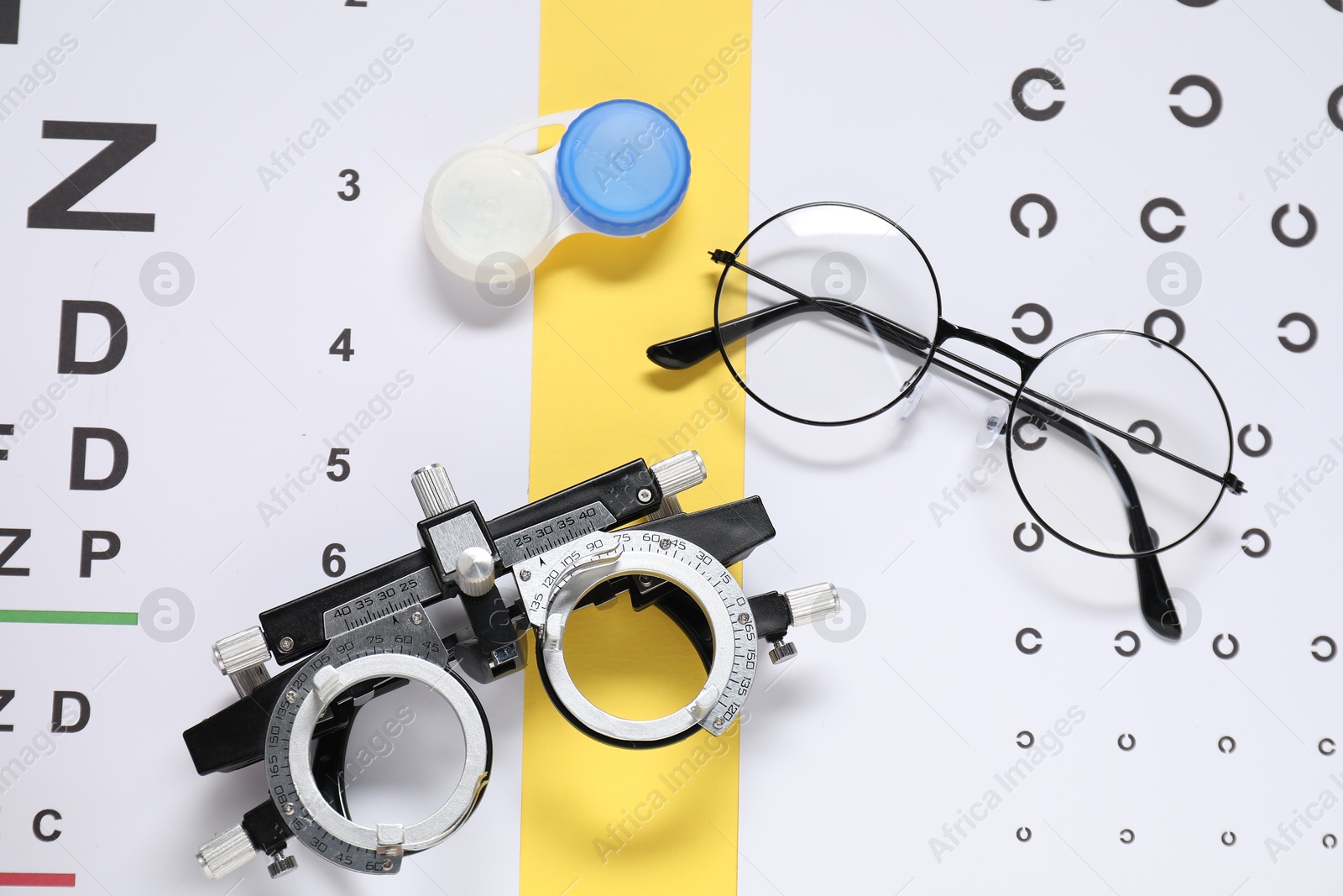 Photo of Glasses, trial frame, vision test charts and lenses on yellow background, flat lay