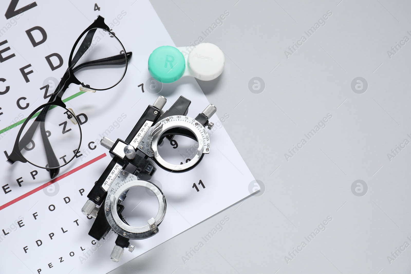 Photo of Glasses, trial frame, lenses and vision test chart on gray background, flat lay. Space for text