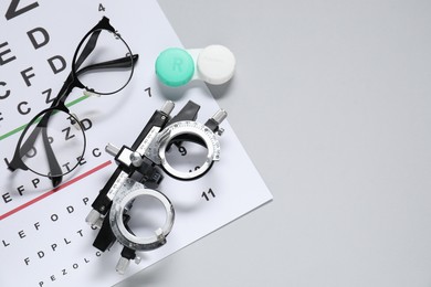 Photo of Glasses, trial frame, lenses and vision test chart on gray background, flat lay. Space for text