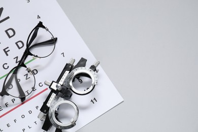 Photo of Glasses, trial frame and vision test chart on gray background, flat lay. Space for text