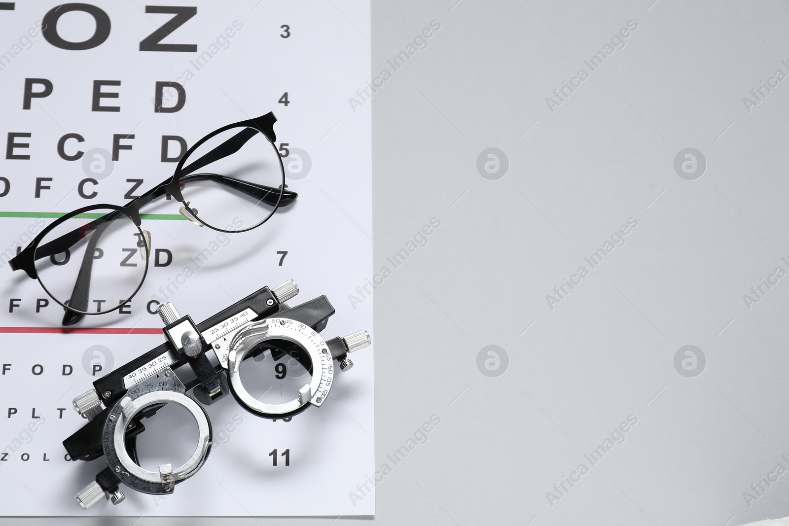 Photo of Glasses, trial frame and vision test chart on gray background, top view. Space for text