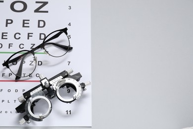 Photo of Glasses, trial frame and vision test chart on gray background, top view. Space for text