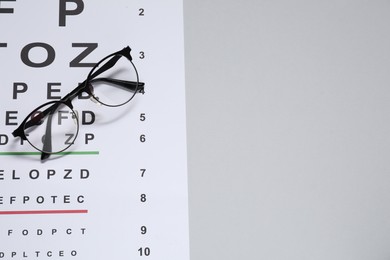 Photo of Glasses and vision test chart on gray background, top view. Space for text