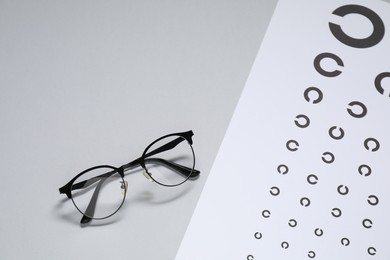 Photo of Glasses and vision test chart on gray background, top view. Space for text