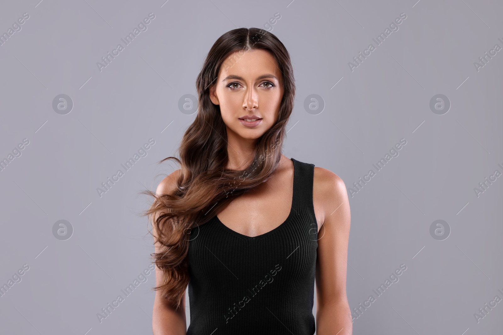 Photo of Hair styling. Portrait of beautiful woman with wavy long hair on grey background