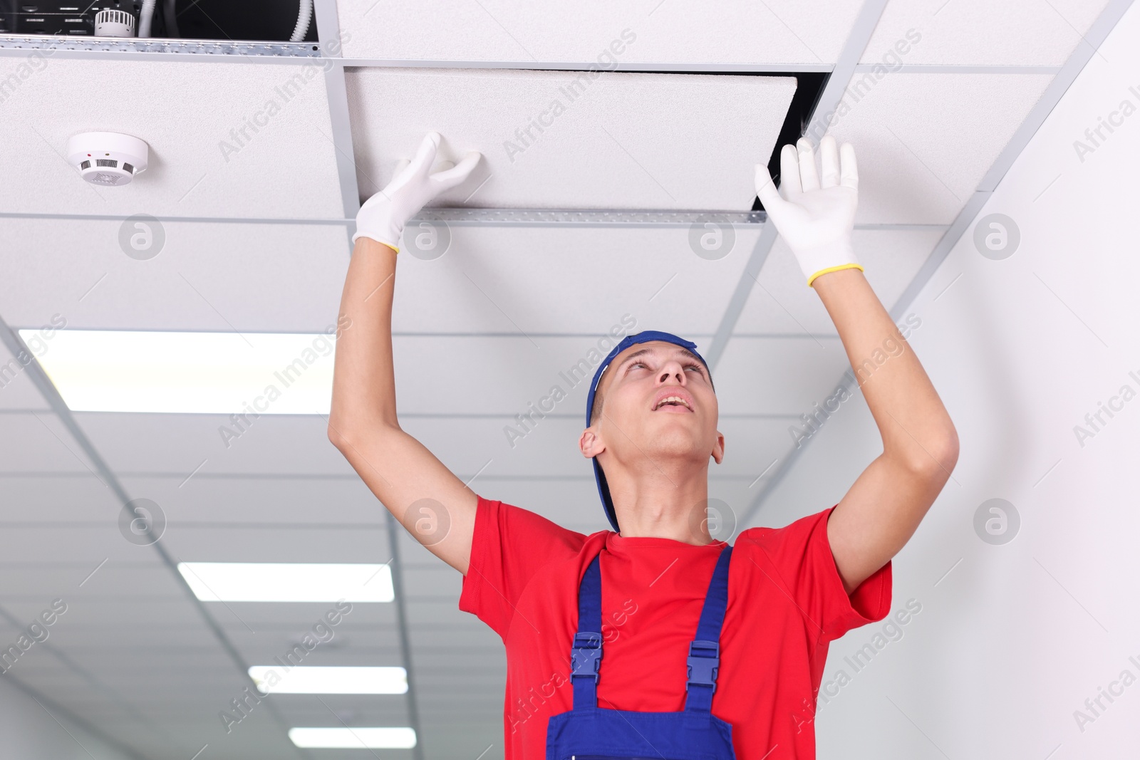 Photo of Suspended ceiling installation. Builder working with PVC tile indoors, low angle view