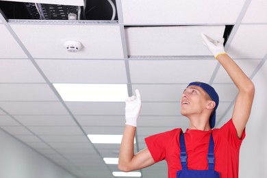 Photo of Suspended ceiling installation. Builder working with PVC tile indoors, low angle view