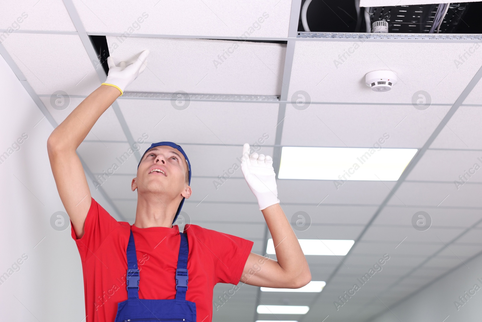 Photo of Suspended ceiling installation. Builder working with PVC tile indoors, low angle view